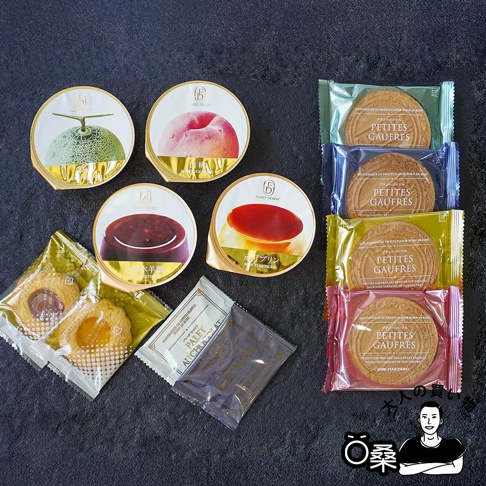 一盒西式甜點禮盒，包含四款獨立包裝的杯裝甜點，分別印有哈密瓜、水蜜桃、紅豆及布丁圖案。另有兩組獨立包裝的餅乾，以及兩包顏色深淺不同的長方形小點心。