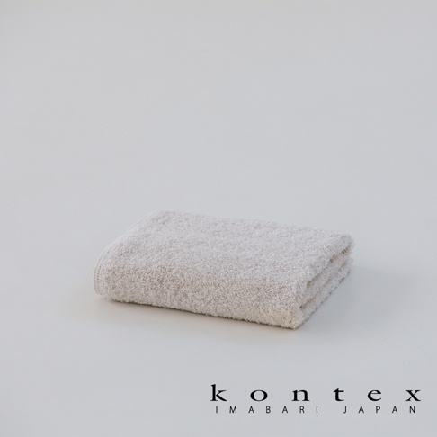一張淺米色的 KONTEX 日本今治製方巾整齊摺疊放置在白色背景中央，毛巾表面呈現柔軟蓬鬆的質感，右下角印有黑色的 KONTEX IMABARI JAPAN 品牌標誌。