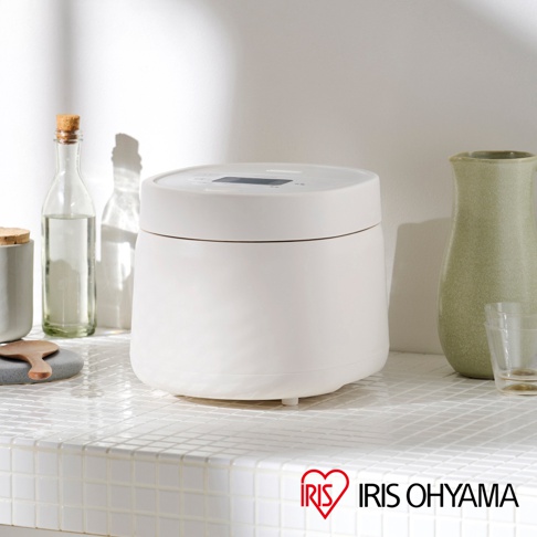IRIS OHYAMA 的白色電子鍋，放置於有白色網格紋理檯面的廚房檯面上，背景有綠色陶罐和玻璃瓶。