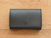 黑色皮革製的寬版證件收納夾，以縫線勾勒出簡約的輪廓，質感樸實，置於木紋背景上。