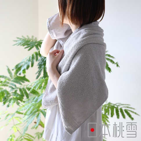 一位女性用灰色薄手迷你浴巾擦拭臉部，浴巾覆蓋在肩上。