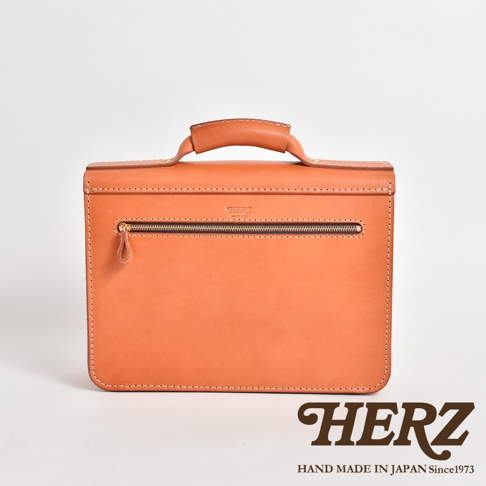 橘色皮革製成的商務公事包，正面有一個拉鍊口袋，頂部有皮革提把，縫線清晰，品牌標誌壓印在上方，整體設計簡約。