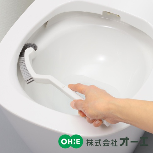 白色塑料手柄的彎曲清潔刷，刷毛為灰色，正被手持清潔馬桶邊緣。