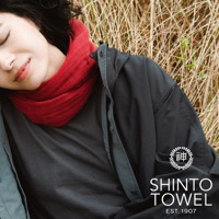 一位女性臉部特寫，身穿紅色針織圍巾、灰色上衣和深灰色外套，背景為乾枯的草叢。