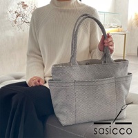 一位身穿米白色高領毛衣的女性，手提一個黑色和白色細小格紋圖案的三河木綿刺子織手提托特包 L，包包外側有兩個方形口袋。