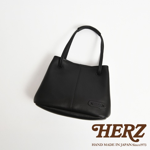 HERZ 黑色皮革手提包，上有品牌壓印 logo，標示「HAND MADE IN JAPAN Since1973」。