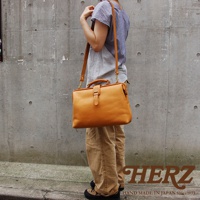 駝色皮革軟式杜勒斯包，採用職人手作工藝，配有可調節的長肩帶和頂部提把，包身設有皮扣開合。