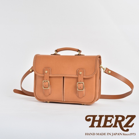 棕褐色皮革製成的手提單肩兩用包，附有可調節肩帶、金色扣環和手柄。包身有縫線裝飾，風格簡約。