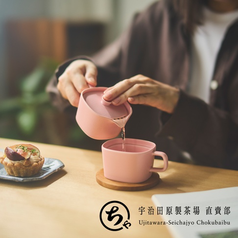 一位穿著深褐色上衣的女性正在將茶水倒入粉紅色的美濃燒杯中，桌面擺放著一小盤精緻的無花果塔。畫面角落顯示宇治田原製茶場直賣部的品牌標誌，整體營造出溫馨靜謐的午茶時光氛圍。