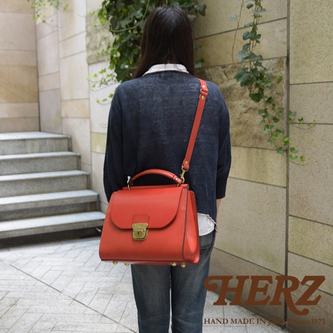 日本HERZ職人手作皮革屋瓦風兩用單肩包，採用紅色硬皮革製作，可手提、肩背、斜背，配有金色鎖扣和鉚釘，包款底部寬敞，可收納B5筆記本與平板，適合日常通勤與外出使用。