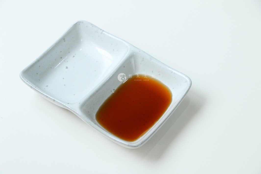 一個淺灰色、帶有細微斑點的陶瓷雙格醬料碟，其中一個格中盛有深棕色的壽喜燒沾醬。
