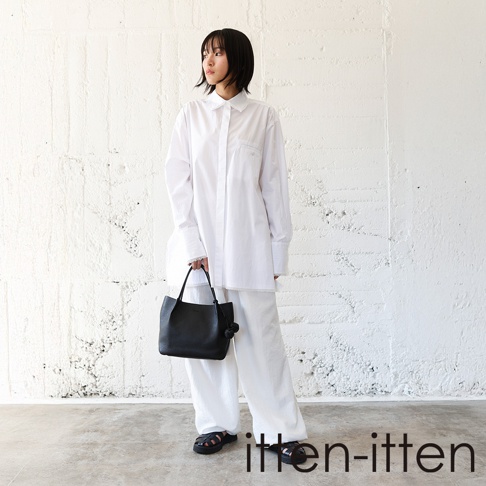 itten-itten 品牌 logo 於圖片右下方，一位身穿寬鬆白色襯衫與白色長褲的亞洲女性，提著黑色皮革托特包，站立於白色紋理牆面和灰色水泥地板前。