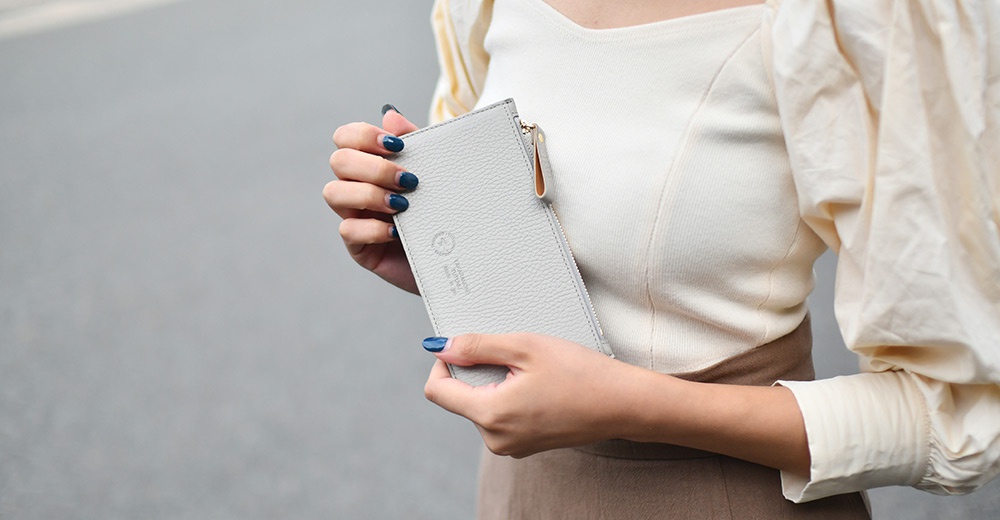 TUTUMU 義大利皮革長夾，由一雙手指輕握，頂部有拉鍊細節