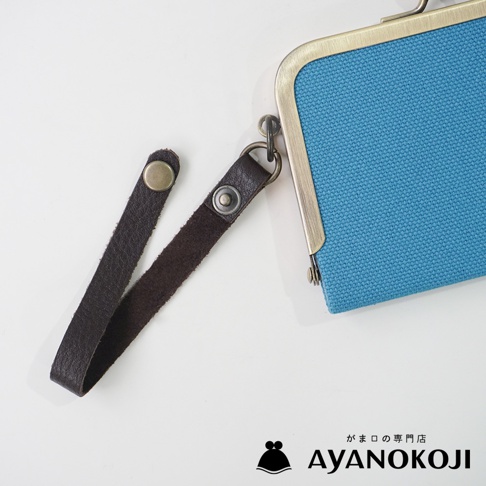 一個深棕色皮革腕帶，一端有一個鉚釘，另一端有一個金屬扣環，連接到一個藍色帆布製成的口金包，包的邊緣是仿古銅色。