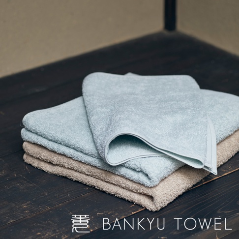 疊放的兩條毛巾，一條為淺藍色，一條為淺棕色，毛巾表面有細緻的長纖維，質地柔軟。