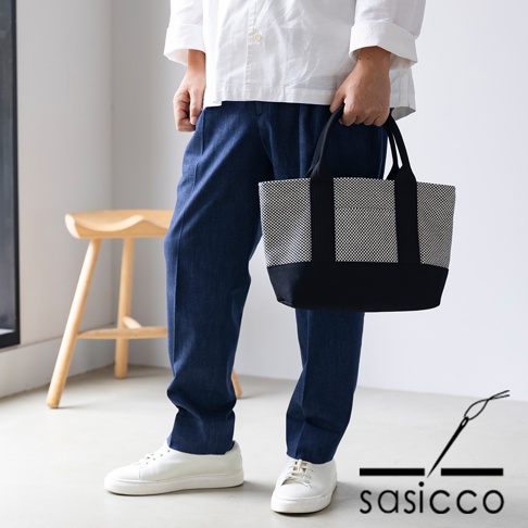 一手提著三河木綿刺子織OBI迷你托特包，包身採黑白格紋與黑色拼接設計，配有黑色提把。