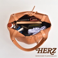 職人手作皮革球形肩掛托特包，焦糖棕色，內部裝有手機、錢包、鑰匙包、水瓶及衣物。