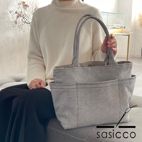 一位身穿米白色高領毛衣的女性，手提一個黑色和白色細小格紋圖案的三河木綿刺子織手提托特包 L，包包外側有兩個方形口袋。