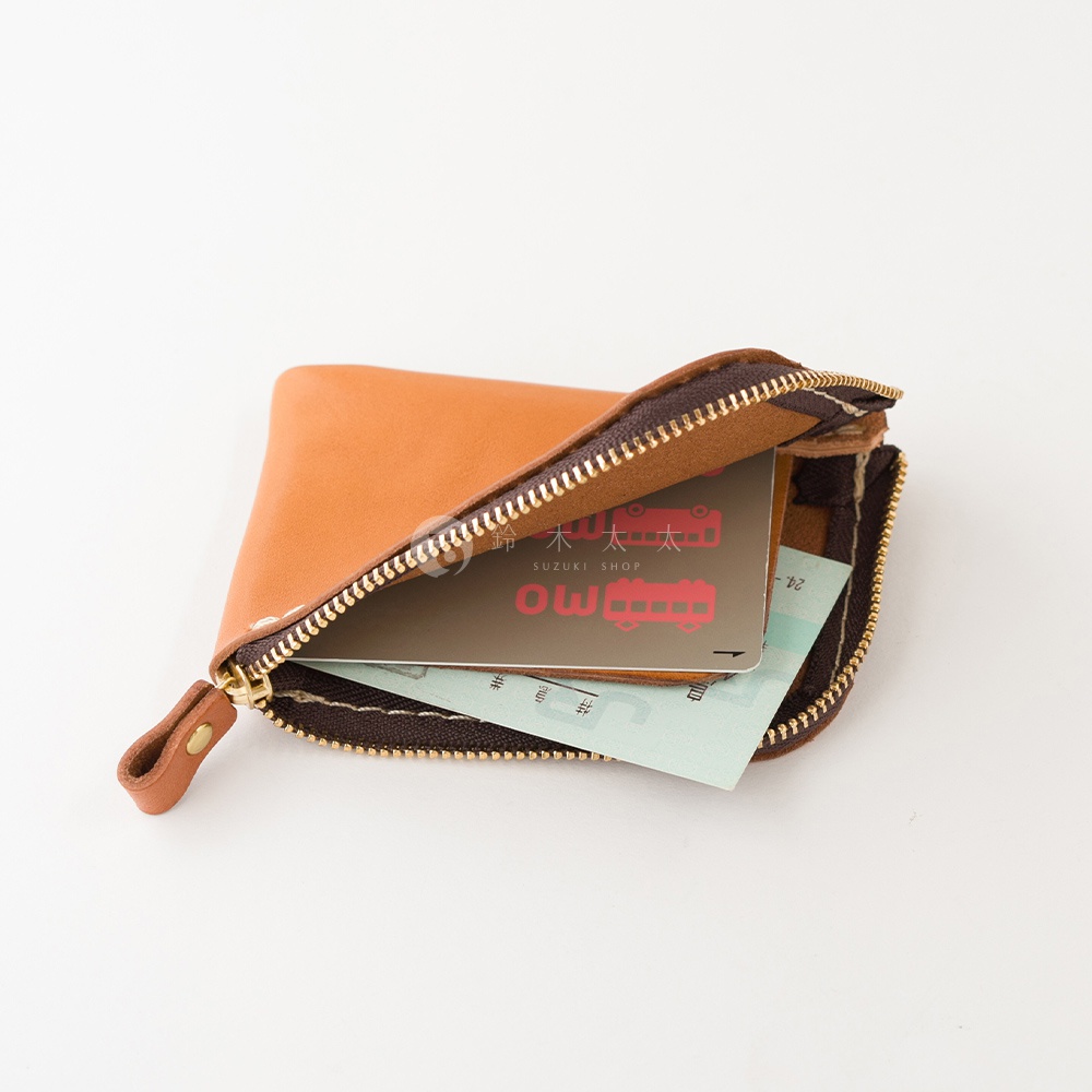 一個棕色皮革製成的日本HERZ迷你收納零錢包，側面以拉鍊開合，內部裝有鈴木太太SUZUKI SHOP字樣的卡片與紙鈔，展示其簡約精巧的設計與質感。