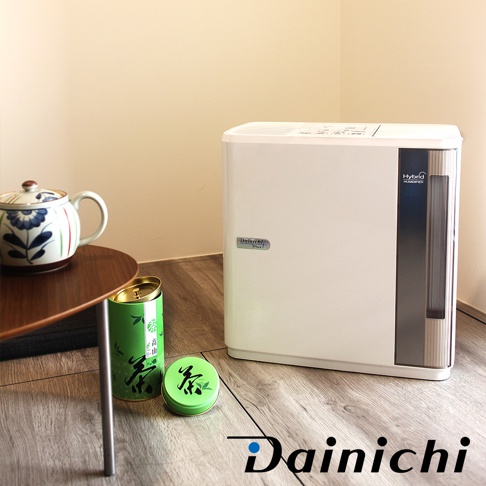 一台白色Dainichi Hybrid Humidifier，側面有灰色面板和水指示窗，左側有綠色茶葉罐和茶葉盒，以及一個帶有藍色花紋的白色茶壺。