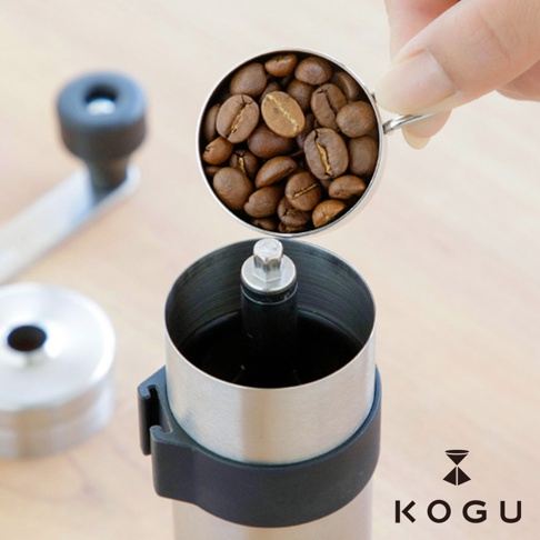 日製18-8不鏽鋼手搖咖啡磨豆器，上方裝有咖啡豆的銀色量杯，磨豆器主體為銀色不鏽鋼材質，搭配黑色塑膠固定環。