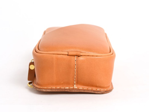 職人手作皮革兩用直立型斜背包 (F-103)，側邊視角，呈現淺棕色天然皮革材質，包身線條圓潤，縫線清晰，底部邊緣有明顯的皮革層疊和縫製細節，左側有金屬釦環和皮革吊飾。