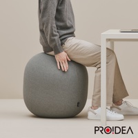 一個灰色的針織收納彈力平衡球，球體呈橢圓形，表面有細緻的織紋，上方坐著一位穿著灰色毛衣和米色長褲的人，手搭在球體上。