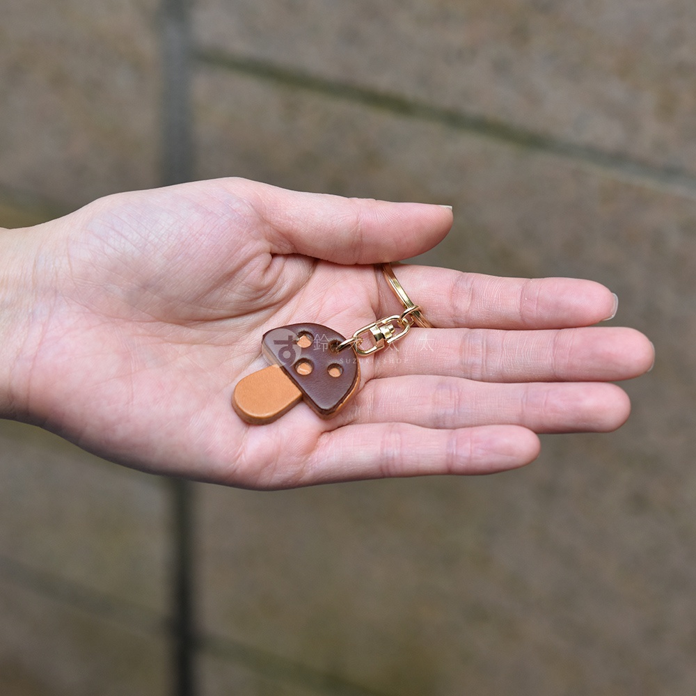 職人手作皮革香菇造型鑰匙圈，菇傘為深咖啡色皮革，印有數字「70」及兩個小圓孔；菇柄為淺棕色皮革，搭配金色鑰匙圈。