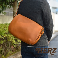 職人手作皮革復古翻蓋郵差包，採用棕色皮革製作，配有可調節式肩帶和金屬扣環，風格簡約，適合日常攜帶。