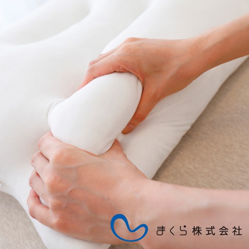 一雙手正在輕柔地擠壓一個純白色的、觸感柔軟的枕頭，枕頭呈現出波浪狀的設計，材質看起來是細緻的布料。