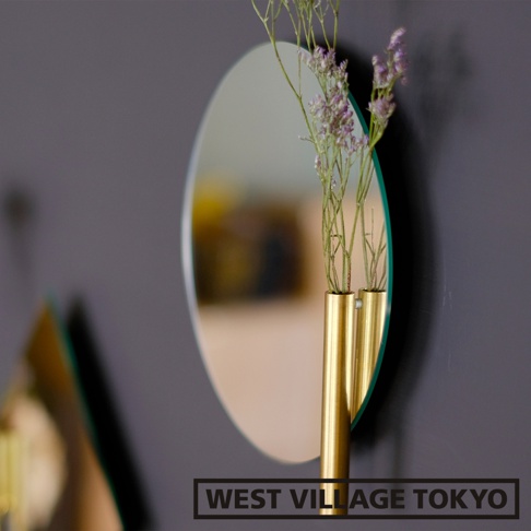 壁掛式圓形鏡面，搭配兩個金色圓柱形單輪花器，插有乾燥的紫色小花，背景為深灰色牆面。