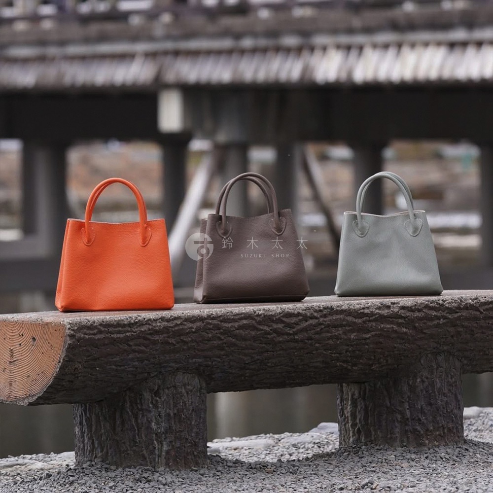 三款京都職人手作手提托特包，分別為亮橘色、咖啡色及淺灰色，皆為皮革材質，設計簡潔，附有提把。