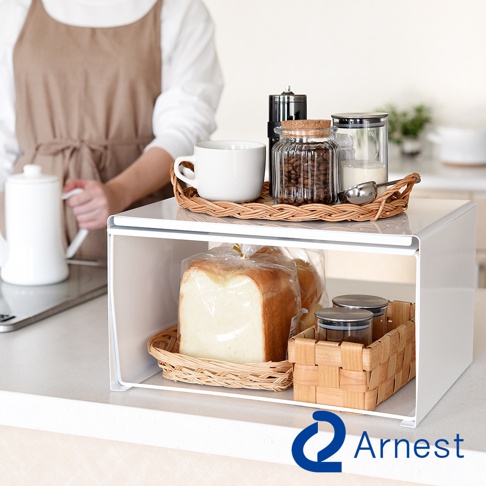 白色金屬廚房收納架，上方擺放著藤編托盤，上面有咖啡豆罐、牛奶罐、白瓷杯和咖啡研磨機。下方則收納著兩條吐司麵包和兩個小玻璃罐，整體呈現簡潔實用的風格。