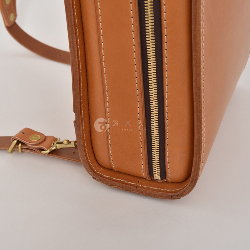 職人手作皮革商務電腦後背包，展示品牌標誌的淺棕色皮革材質，搭配金色拉鍊和皮革肩帶，縫線清晰，細節精緻。