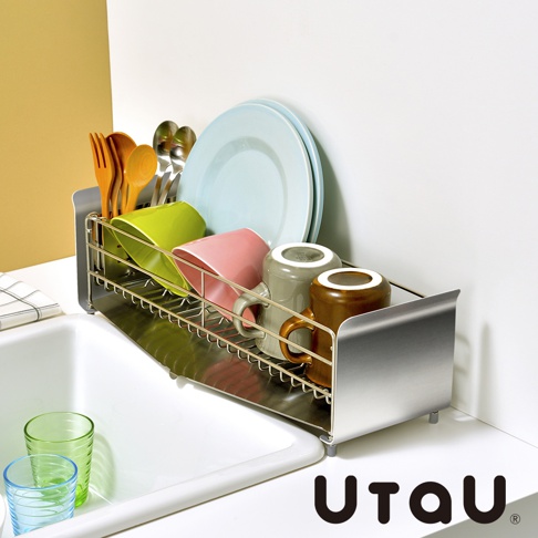 不鏽鋼窄型碗碟瀝水架，附有瀝水盤，架上擺放著木製餐具、綠色與粉紅色杯子、灰色與棕色馬克杯，以及兩個淺藍色盤子。