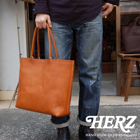 一名男子身穿牛仔褲，手提一個棕色皮革托特包，包包的縫線清晰可見。