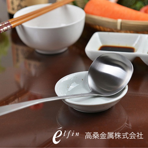 日製不鏽鋼湯杓，勺頭呈圓弧形，勺柄細長。湯杓置於白色陶瓷小碟上，背景有白色碗、筷子、醬油碟及胡蘿蔔。