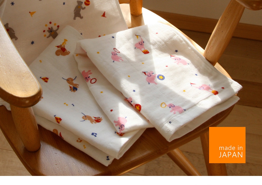 白色紗布毛巾，印有可愛的馬戲團主題圖案，包括玩耍的小熊、小象和馬戲團小丑。材質輕柔，適合嬰兒使用。