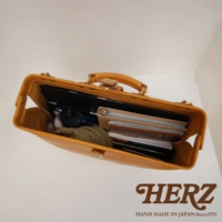 職人手作皮革軟式杜勒斯包，淺棕色皮革，包內裝有筆記本、文件夾、筆記型電腦和保溫杯。