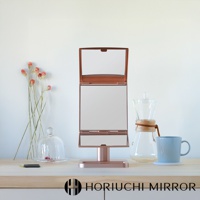 玫瑰金色桌上型三折化妝鏡，鏡面可360度旋轉，附有底座，擺放在木質檯面上，背景為白色牆面，旁有乾燥花束、玻璃罩盅、咖啡壺和藍色馬克杯。