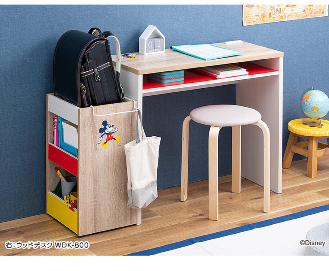 迪士尼系列木質收納櫃，木紋色，附有滾輪，正面有米奇圖案，側邊有白色帆布袋。收納櫃內有紅色、黃色和藍色隔層，擺放有書本、鉛筆和背包。