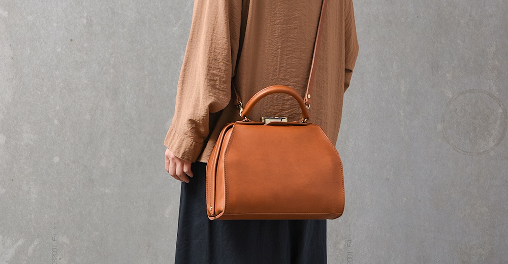 棕色皮革手提包，具備金色口金開合、頂部提把及可拆卸斜背帶。