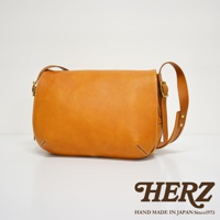 職人手作皮革復古翻蓋郵差包，採用天然棕褐色皮革製成，帶有細緻的縫線和金屬搭扣。包款設計簡約，翻蓋式開口，適合日常攜帶。