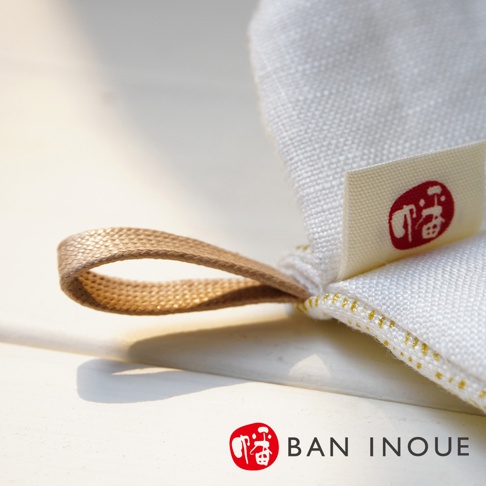 Tricot 棉麻防燙鍋套，白色布料，帶有金色縫線及棕色掛環。布料上縫有白色標籤，印有紅色「福」字圖案。