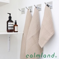 三條米色無撚紗質長方巾掛在牆上的掛鉤上，左側架子上擺放著兩瓶棕色瓶裝的洗浴用品。