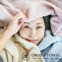 女性臉部被柔軟的有機棉浴巾圍繞，浴巾呈現粉色、奶油色和淺藍色。