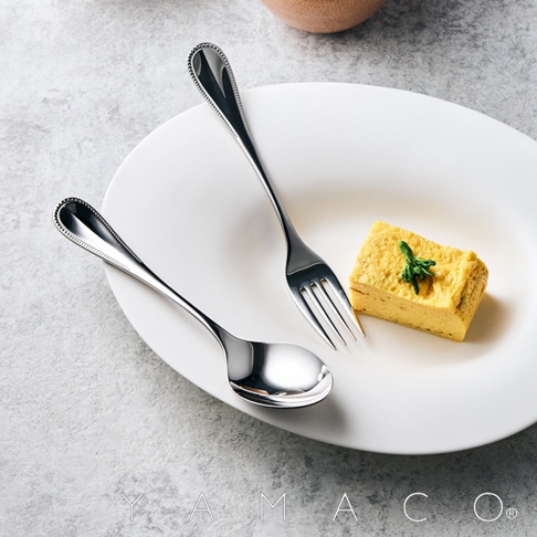 不鏽鋼叉匙組，叉子與湯匙的握柄處有細緻的滾珠裝飾，盤中擺放著一塊日式煎蛋捲。