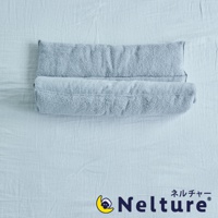 淺灰色毛巾材質的捲捲枕，柔軟蓬鬆，呈現出雙層捲繞的設計，放在淺藍色床單上。