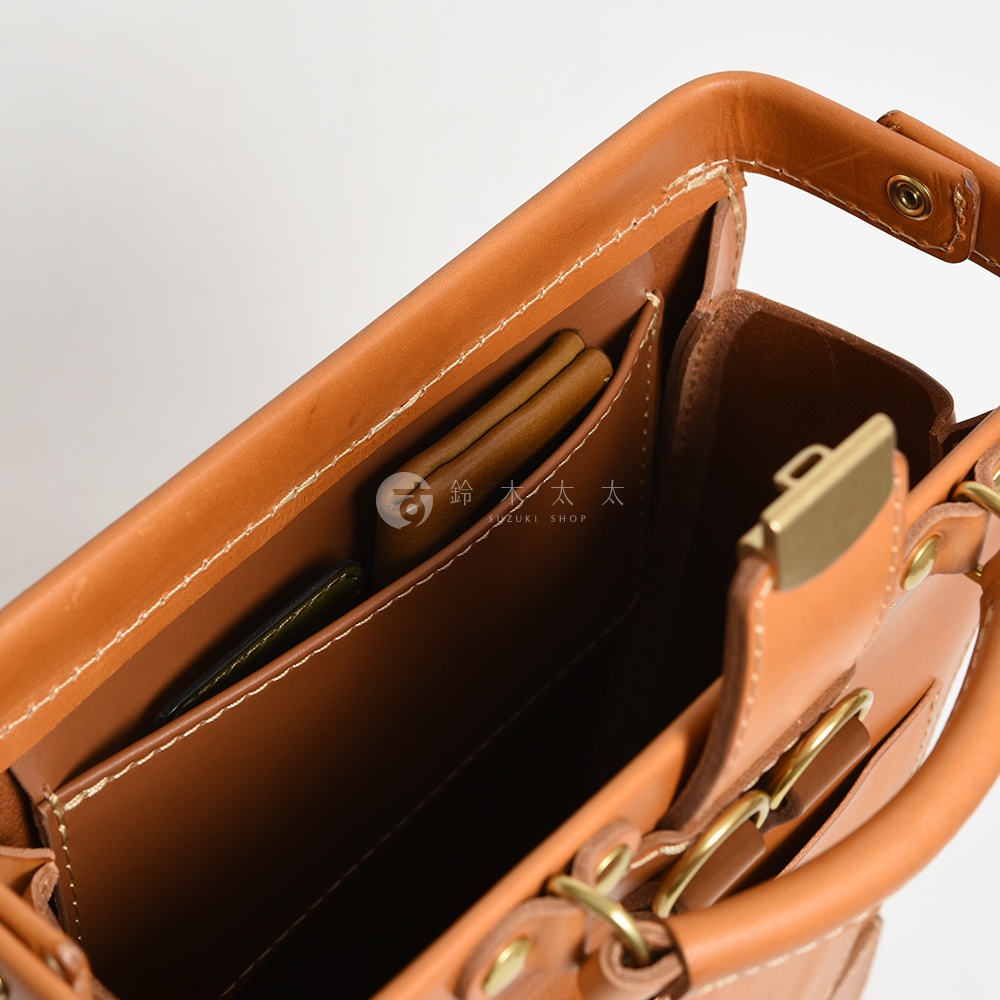 職人手作皮革杜勒斯商務後背包 BJ-10，展示其內部結構，包含淺棕色皮革隔層，置有卡夾及筆。包體為淺棕色皮革，搭配金色金屬扣具與車縫線。