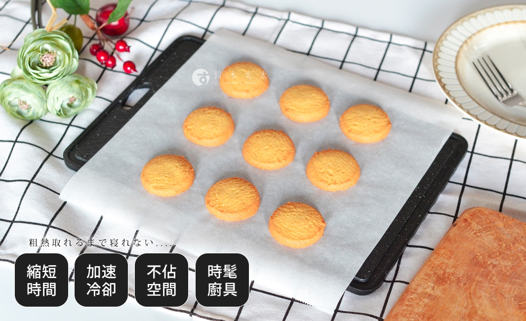 黑色食物快速冷卻盤，上面鋪著烘焙紙，擺放著九個金黃色的圓形餅乾。盤子旁有餐盤、叉子、裝飾用的綠色花朵和紅色漿果。